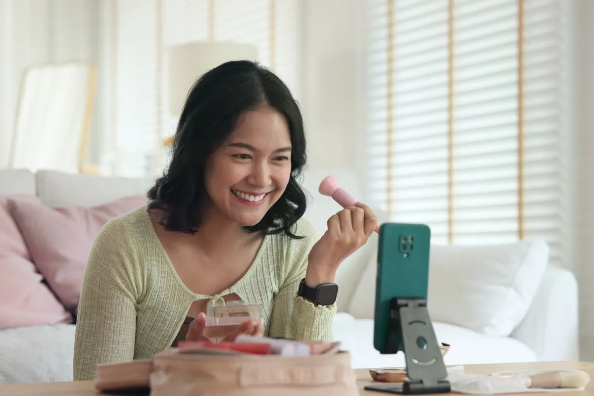 young woman films herself on phone, doing makeup